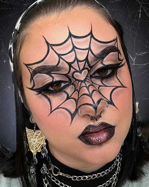 Dramatic Halloween makeup showcasing a large spider web above a smooth foundation and deep, glossy vampy lips.