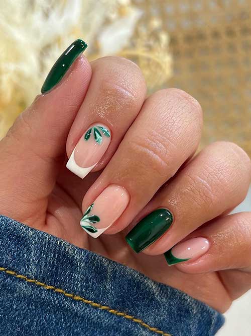 Glossy dark green nails featuring white French tips and green leaf accents for a stylish and nature-inspired look.