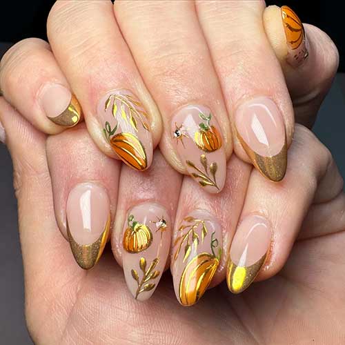 Gold chrome French fall nails on a nude base, featuring accent nails with gold pumpkins and leaf designs.