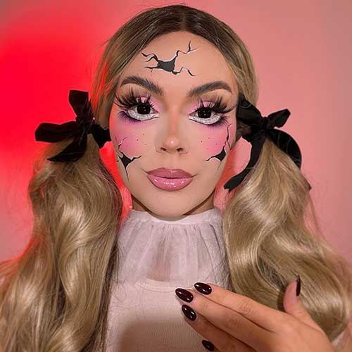 Halloween makeup featuring a broken doll look with pink eyeshadow, glossy pink lips, and black nails.