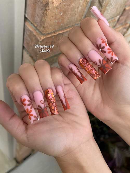 Long matte nude pink nails featuring autumnal designs, including pumpkins, stitch French tips, flowers, and a pumpkin spice glitter accent.