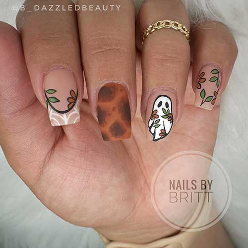 Short nude nails embellished with autumn-themed nail art in green and brown, showcasing floral, tortoise, and ghost designs.