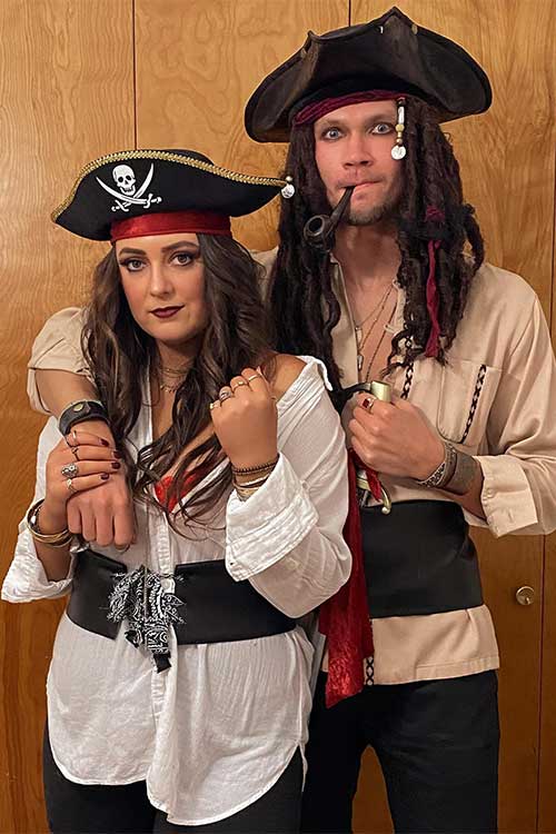 A pirate couple dressed in elaborate costumes, complete with hats, eye patches, and accessories, ready for a Halloween party.