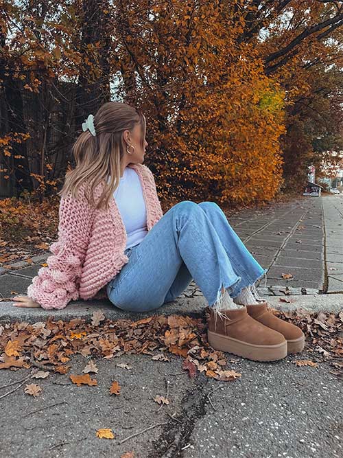 A cozy outfit featuring a chunky knit sweater over a lightweight top, high-waisted jeans, and ankle boots in warm fall tones.