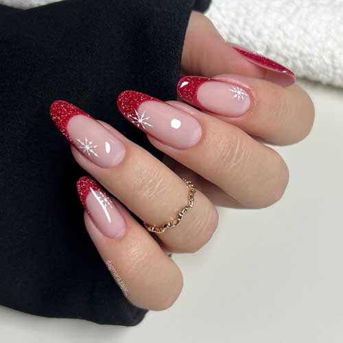 Long almond-shaped French red Christmas nails with glitter on a nude base, featuring white snowflakes on each nail.