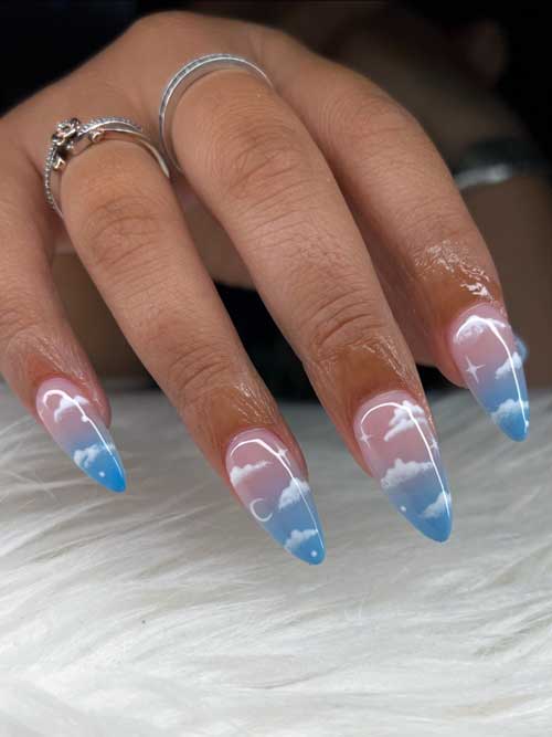 Almond-shaped blue ombre nails featuring white clouds and stars, creating a dreamy and celestial aesthetic.