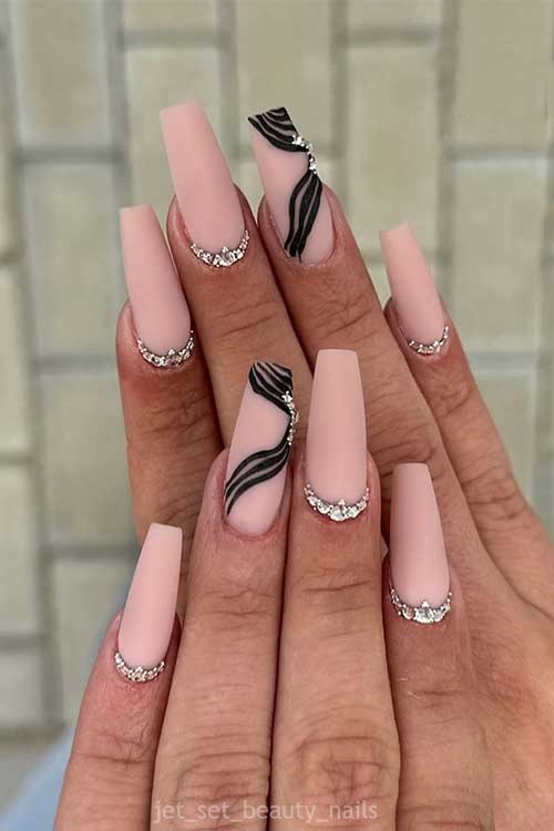 Long matte coffin nude nails with silver glitter at the cuticles and an accent nail featuring black gel lines and rhinestones.