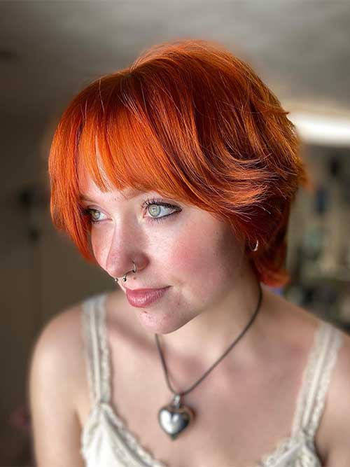 A stylish short shag haircut in copper color, featuring a trendy fringe that frames the face elegantly.