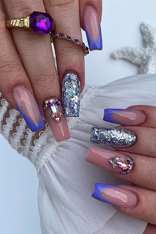 Long coffin-shaped purple French tip nails with a nude accent nail adorned with rhinestones and a silver glitter accent nail