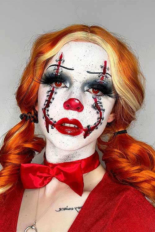 Pennywise-inspired Halloween makeup showcasing a stitched smile, glossy red lips, a red nose, and vivid red contact lenses.