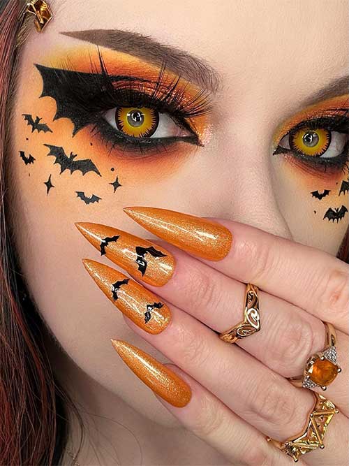 Stunning Halloween eye makeup with bat wing eyeliner, vibrant orange to yellow eyeshadow, and small bats on the cheek.