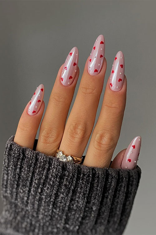 Glossy nude almond-shaped gel nails adorned with tiny white pearls and red heart shapes