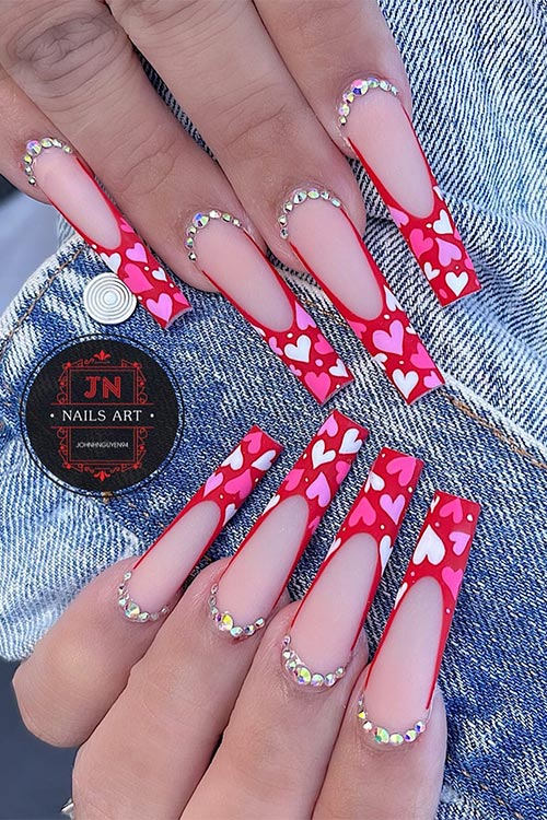 Long coffin-shaped matte red French nails with white, pink, and lilac tiny hearts adorned with rhinestones