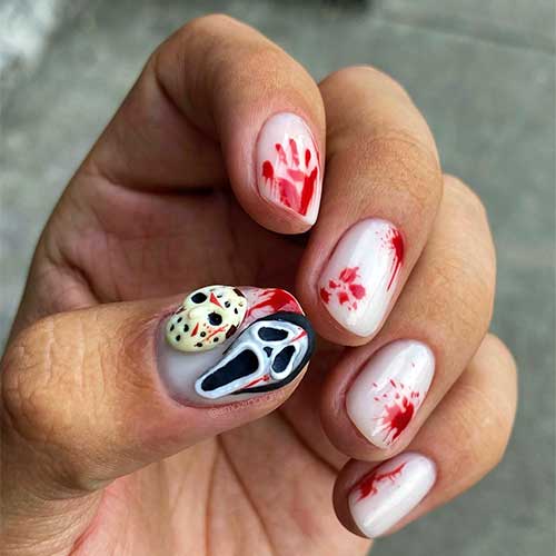 Milky white Halloween nails with blood splatter art, featuring 3D scary faces on the thumb for a chilling Halloween look.