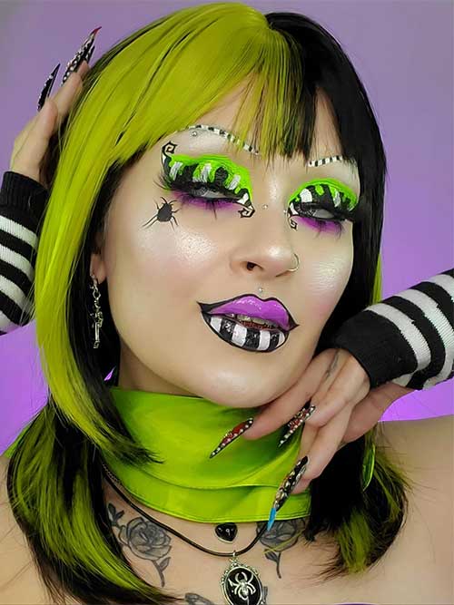 A creative Beetlejuice makeup look featuring black and white eyeshadow, neon green crease, and a spider on the cheek.