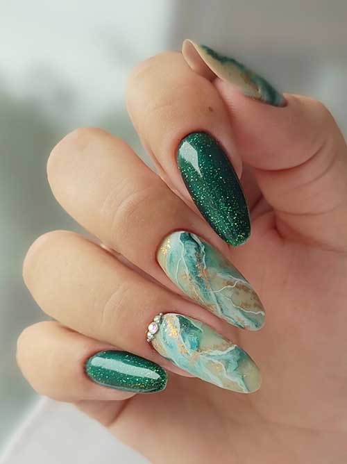 Green marble nails with gold glitter and rhinestones on the ring finger, complemented by two accent nails featuring glitter.