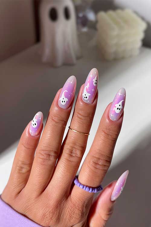 Long almond-shaped nails in purple and white, adorned with white stars and small ghost designs.