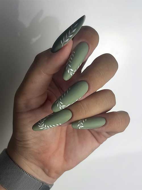 Long almond-shaped olive green nails featuring intricate white leaf designs for an elegant and stylish look.