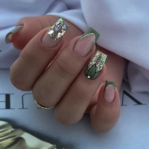 Olive green coffin-shaped nails featuring gold glitter, black leaf art on one accent nail, and foil shreds on another.