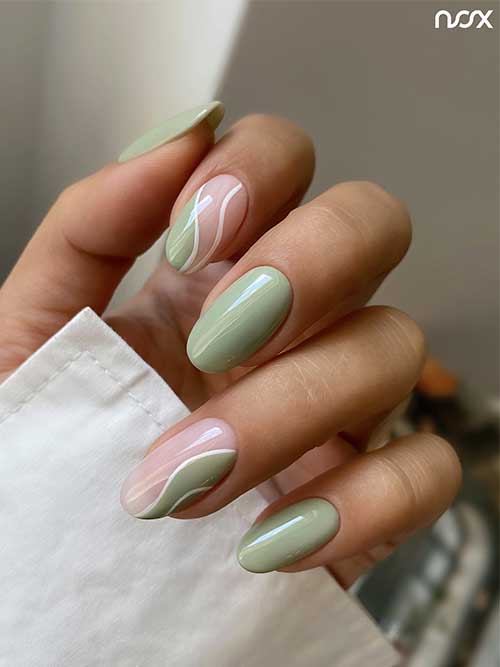 Sage green nails with two accent nails featuring white swirls and negative space on a nude pink base.