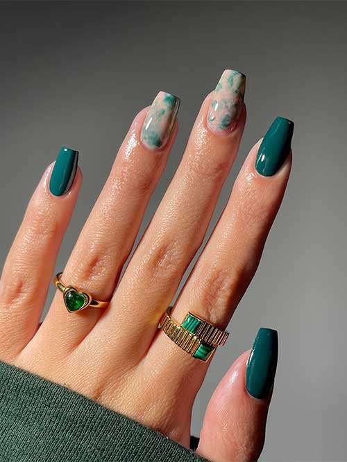 Stunning emerald coffin nails complemented by two green marble accent nails set against a nude base for a chic look.