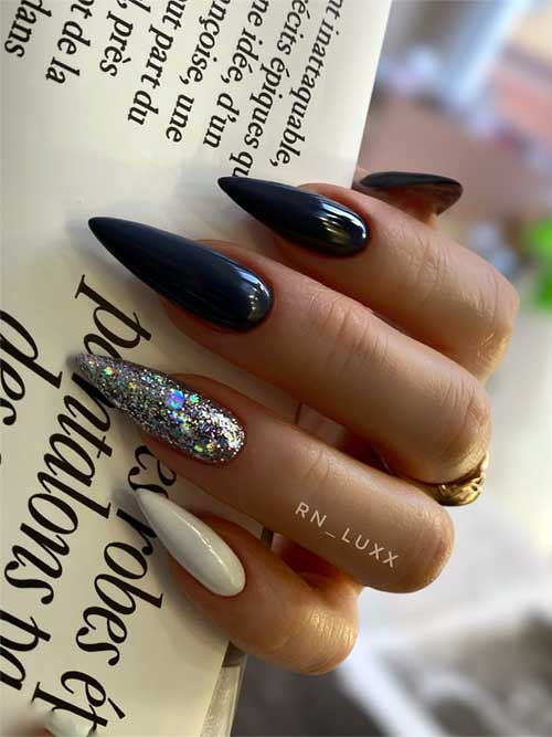 Long glossy black stiletto nails with a white accent and a silver glitter accent nail, perfect for a stylish fall look.