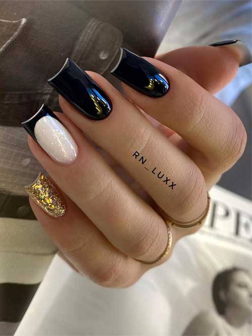 Long square black nails with a French tip over a milky white base, featuring a gold glitter accent nail with foil flakes.