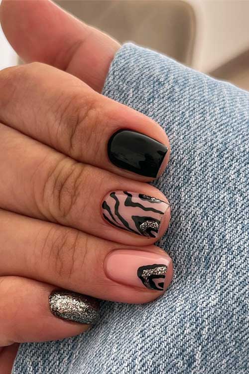 Short fall black nails with two nude nails featuring black zebra prints and silver glitter, plus a silver glitter pinky nail.