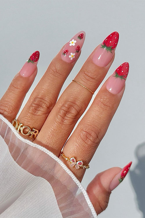 Almond-shaped nude pink nails with strawberry French tips and a nude pink accent adorned with tiny flowers and strawberries
