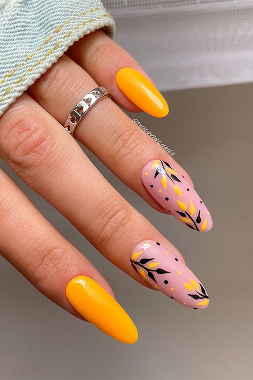 Long almond-shaped neon orange nails with two accent nails adorned with orange and black leaf nail art and dots