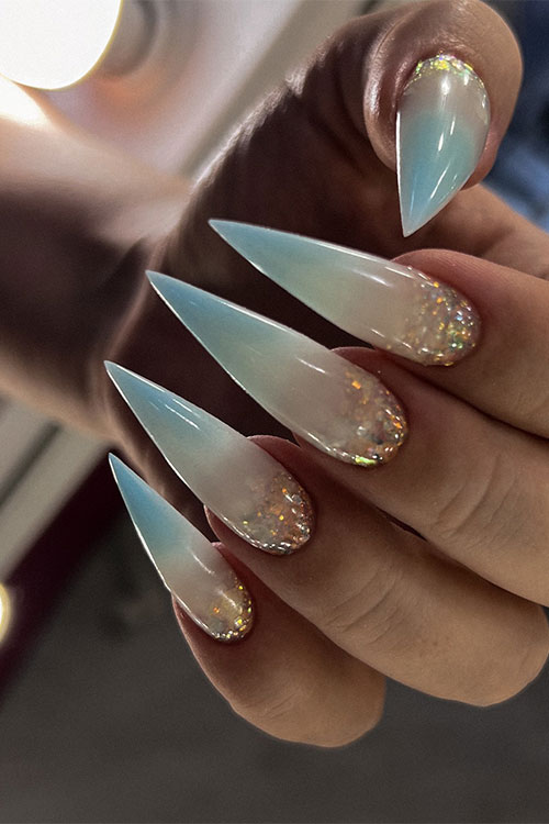 Long stiletto-shaped nude and sky blue ombre nails with encapsulated glitter above the cuticles