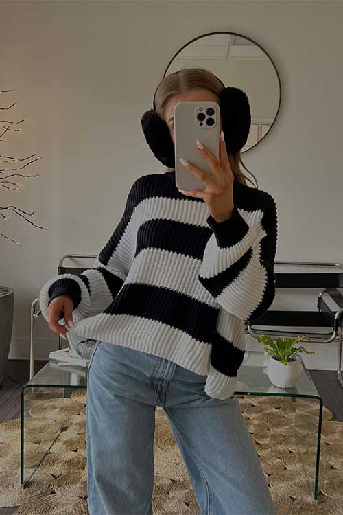 A woman in a stylish striped sweater poses for a selfie, showcasing her fashionable sense of style and confidence.