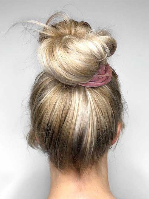 A messy top knot hairstyle with strands falling out, creating a carefree and informal look suitable for everyday wear.