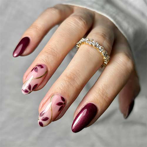 Burgundy gel nails with two nude pink accents featuring floral designs and gold swirls for an elegant look.