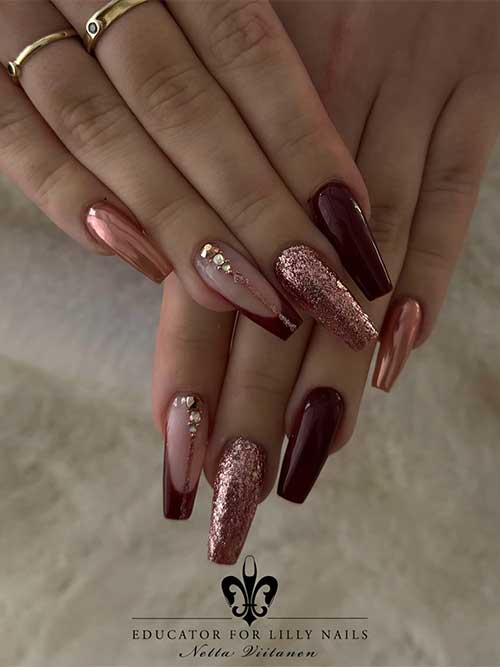 Elegant burgundy nails adorned with chrome rose gold, glitter, rhinestones, and stylish French accents.