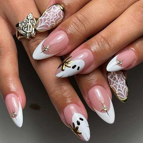 Elegant white Halloween French tips with a ghost accent nail, nude nail with spider web, gold 3D gel, and crystal stars.