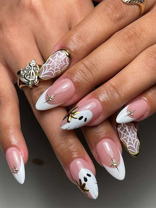 Elegant white Halloween French tips with a ghost accent nail, nude nail with spider web, gold 3D gel, and crystal stars.