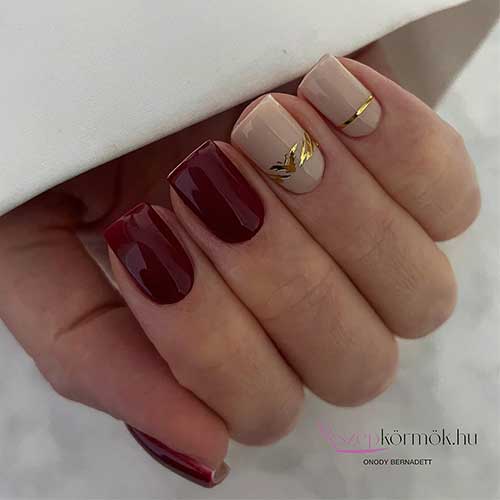 Short burgundy and beige nails featuring elegant gold stripe decorations for a chic and stylish appearance.