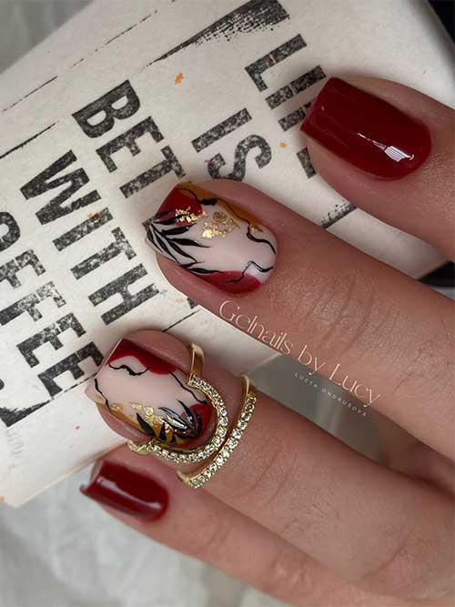 Short burgundy nails featuring abstract art, gold foil accents, and black leaves on two standout nails.