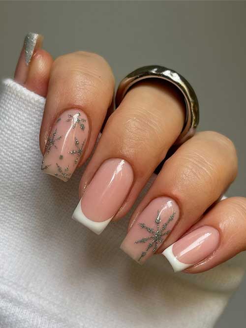 Cute winter nails with white French tips, glitter snowflakes on nude accents, and a silver glitter French thumb nail.