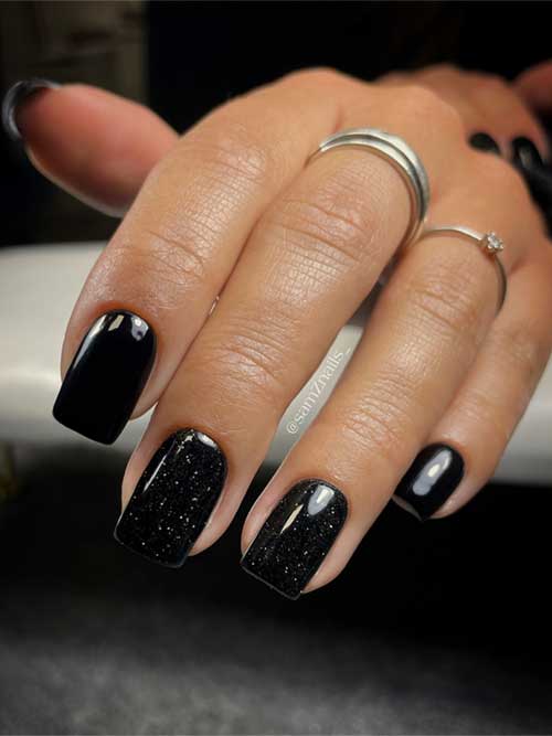 Elegant black square nails complemented by two accent nails adorned with subtle white speckles.