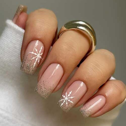 Gold glitter winter nails with glittery tips on a nude base, featuring large snowflakes on two accent nails.