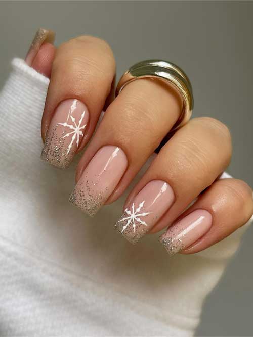 Gold glitter winter nails with glittery tips on a nude base, featuring large snowflakes on two accent nails.