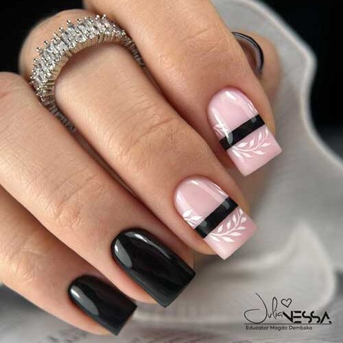 Long fall black nails with a glossy finish, featuring two nude pink accent nails with white leaf art and black stripes.