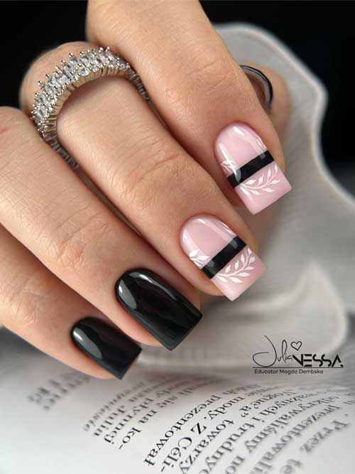 Long fall black nails with a glossy finish, featuring two nude pink accent nails with white leaf art and black stripes.