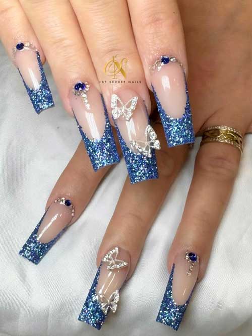 Navy blue French glitter winter nails on a nude base, adorned with rhinestones and butterfly designs for a chic look.