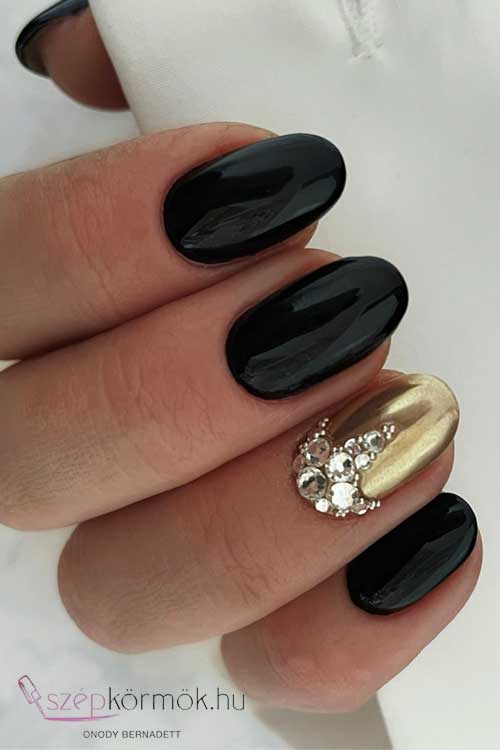 Round black nails with gold chrome accents, adorned with sparkling rhinestones and crystals for a glamorous look.