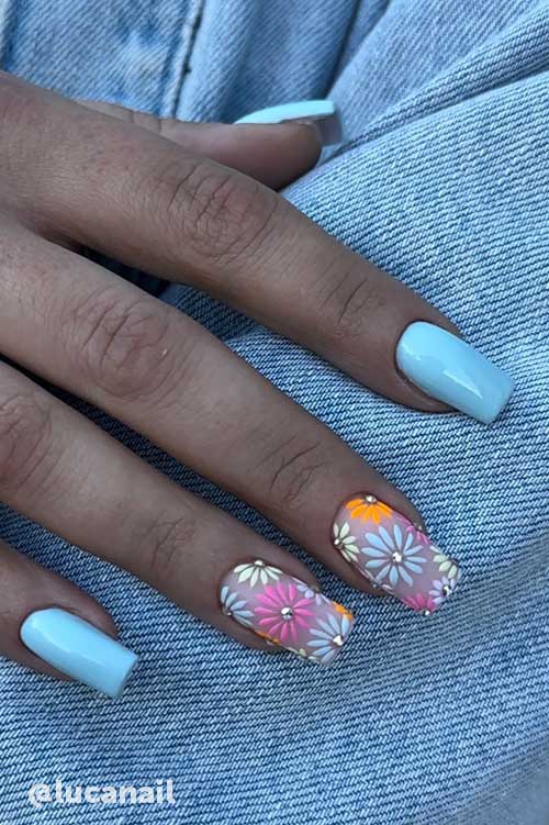 Light blue nails with two accent nails featuring delicate floral patterns of daisies in soft pink, white, yellow, and orange.