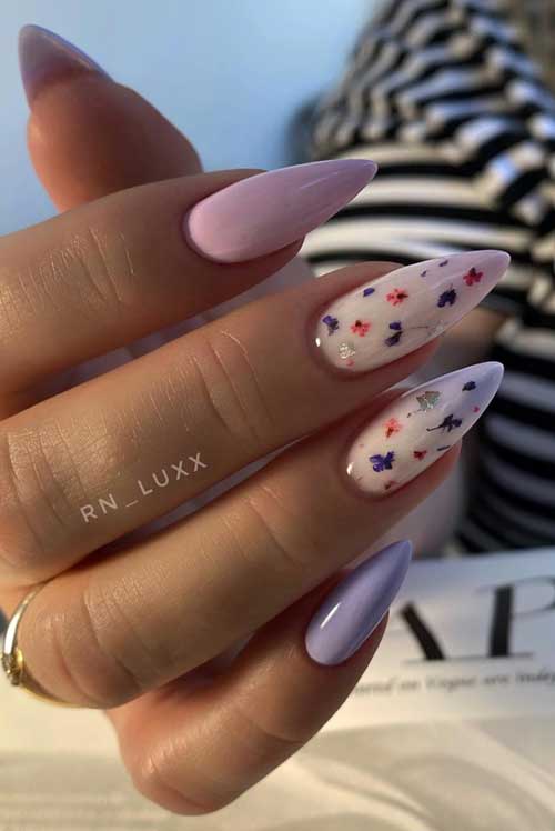 Long, almond-shaped nails in soft pastels with lavender, white, and floral designs, accented by subtle silver sparkles.