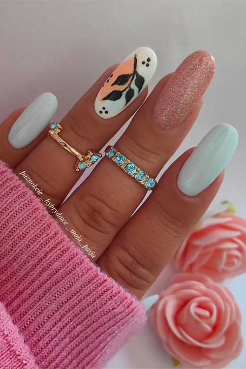 Pastel blue nails with pink glitter, abstract art on the middle finger, pink sweater, and vibrant pink roses in the background.